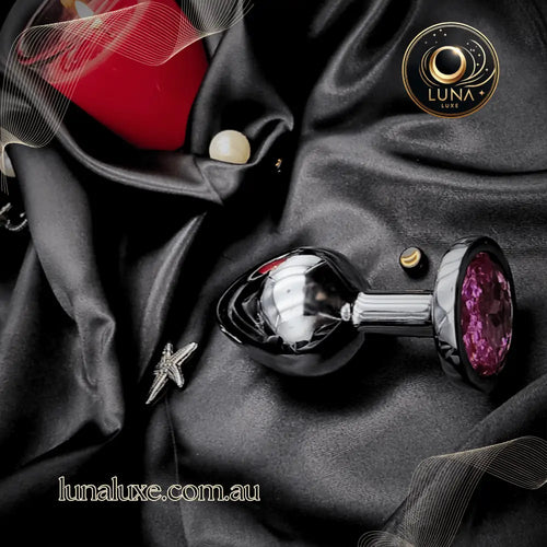 Stainless steel jeweled anal plug on black satin, teardrop shape with faceted pink crystal base.