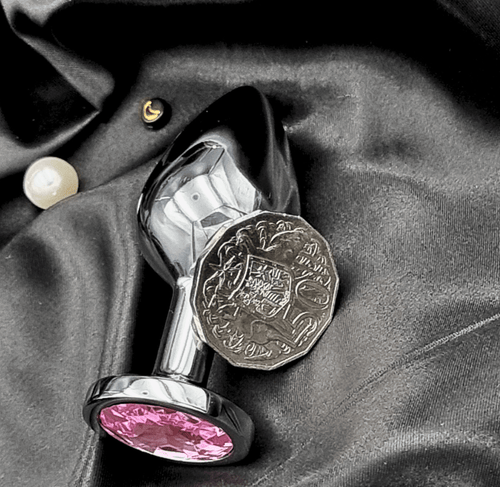 Two sizes of jeweled stainless steel anal plugs on satin, highlighting mirror finish and crystal ends.