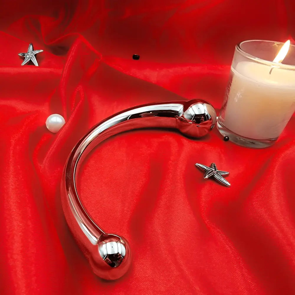 Side view of stainless-steel arc wand beside a candle, showing smooth mirror finish and ergonomic curve.