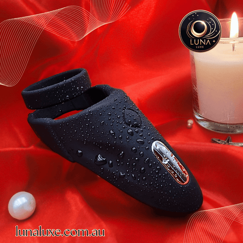 Black vibrating cock ring sleeve on red fabric with water droplets, soft silicone and built-in motor.