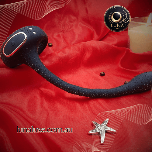 Black app-controlled prostate massager on red satin with water droplets, curved head and perineum arm.