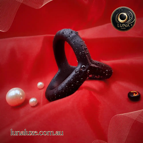 Black triple silicone cock ring on red fabric with water droplets, linked triangular design for shaft and balls.