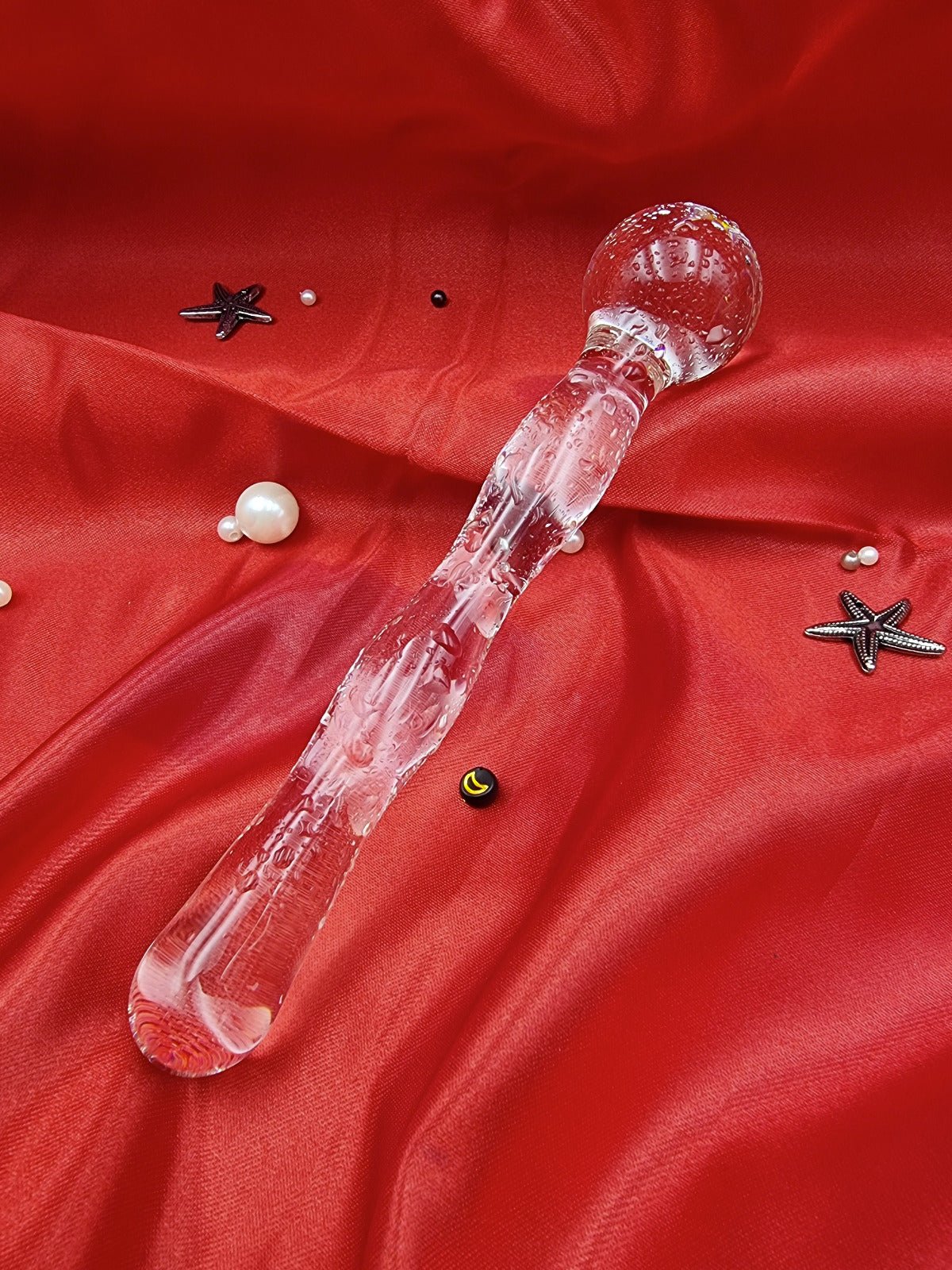 Angled view of the clear glass dildo wand, showing rippled texture and tapered tip on silk fabric.