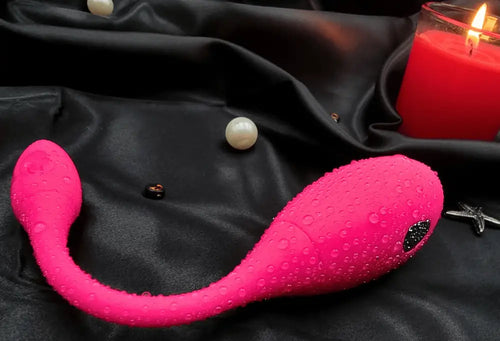 Top view of the wearable vibrator beside a candle, highlighting the curved G-spot arm and external head.