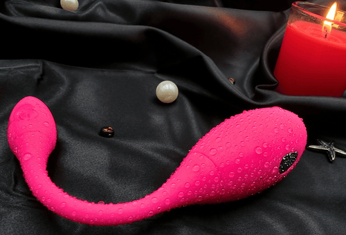 Top view of the wearable vibrator beside a candle, highlighting the curved G-spot arm and external head.