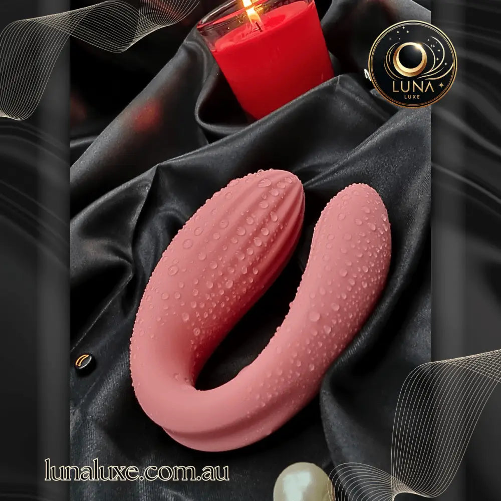 Dusty-rose wearable vibrator on black satin, U-shaped with textured silicone and water droplets.