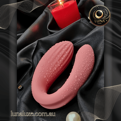 Dusty-rose wearable vibrator on black satin, U-shaped with textured silicone and water droplets.